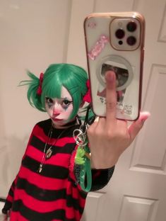 a woman with green hair and makeup holding up a cell phone to take a selfie