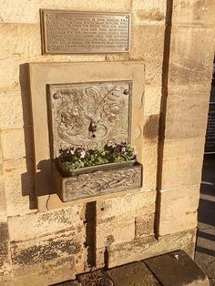 a plaque on the side of a building with flowers growing out of it's sides