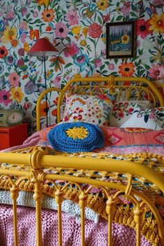 a yellow bed frame in front of a colorful wallpapered room with flowers on the walls