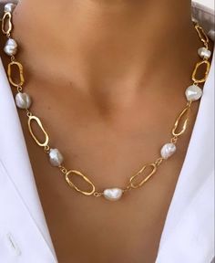 a woman wearing a gold and white necklace with pearls on the link, in front of her chest