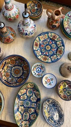 a table topped with lots of colorful plates and bowls on top of a white cloth