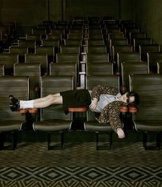 a woman laying on top of a chair in an empty room with rows of chairs