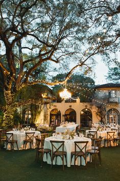 an outdoor dining area with tables and chairs set up for dinner under the trees at dusk