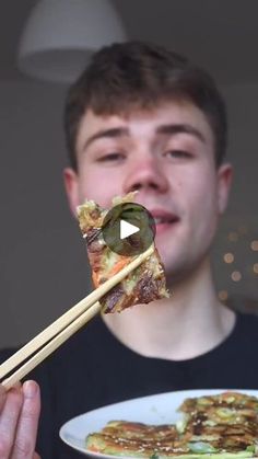 a man holding chopsticks with food on it in front of his face,