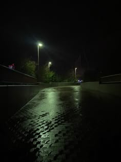 an empty walkway at night with street lights in the background and rain on the ground