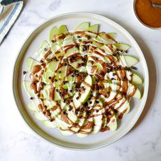 a white plate topped with sliced apples covered in caramel sauce and pecans next to a bowl of dressing