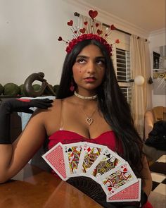 a woman in a red dress is holding two playing cards and wearing a tiara