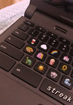 an open laptop computer sitting on top of a white and blue blanket with stickers