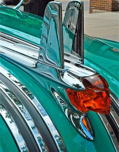 the hood ornament of an old green car is reflected in its shiny chrome finish