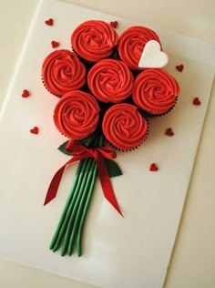 a bouquet of red cupcakes sitting on top of a cutting board next to hearts