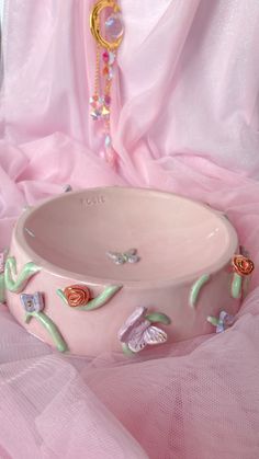 a pink bowl sitting on top of a bed next to a beaded necklace and bracelet