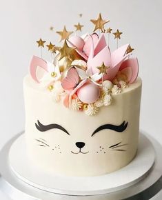 a white cake with pink and gold decorations on it's face, sitting on top of a table