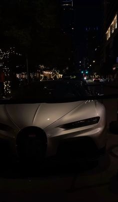 a white car parked on the side of a road at night with buildings in the background