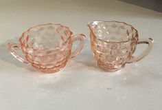 two pink glass cups sitting on top of a white counter next to an orange object