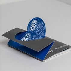 a blue and silver business card holder on a white surface with an image of a peacock in the middle