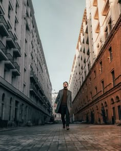 a man walking down the middle of an alley way between two tall buildings with balconies on each side