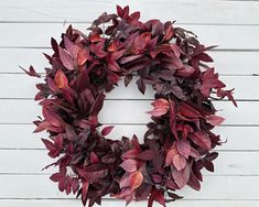 a wreath with red leaves is hanging on a white wooden wall in front of a door