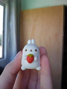 a hand holding a small white toy with a heart on it's nose and an apple in the other hand