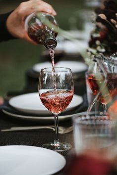 a person pouring wine into a glass on top of a table