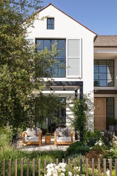 a large white house with lots of windows and plants in the front yard, next to a wooden fence