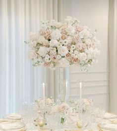 a tall vase filled with white and pink flowers on top of a table covered in plates