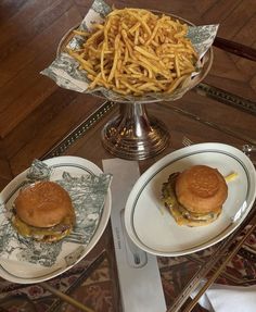 two plates with sandwiches and french fries on them sitting on top of a glass table