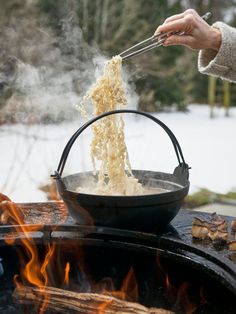 someone is cooking noodles on an outdoor grill in the snow with tongs over it