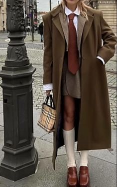 a woman in a coat and tie standing next to a lamp post