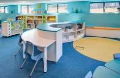 an empty classroom with desks, chairs and bookshelves in the corner on blue carpeted flooring