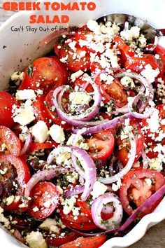 greek tomato salad with onions and feta cheese in a white bowl on a wooden table