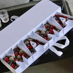 an open white box filled with assorted chocolates and strawberries on top of a table