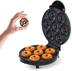 a person holding a donut in front of a waffle maker with six doughnuts on it