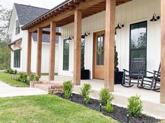 the front porch of a house with rocking chairs and plants on the lawn outside it