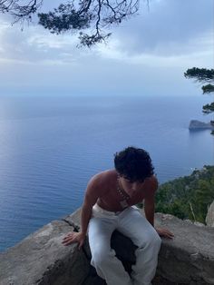 a woman sitting on top of a rock next to the ocean