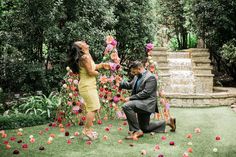 a man kneeling down next to a woman in a yellow dress and holding pink flowers