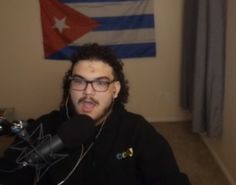 a man wearing headphones sitting in front of a microphone with a flag on the wall behind him