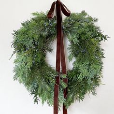 a christmas wreath hanging on the wall with a brown ribbon tied around it and evergreen leaves