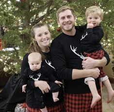 a man and woman are holding their baby in front of a christmas tree with deer antlers on it