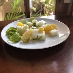 a white plate topped with cut up fruit on top of a wooden table next to a window