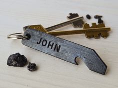 the personalized keychain is next to some rocks and metal keys that say john