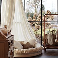 a dog bed in the corner of a room next to a large window with sheer curtains