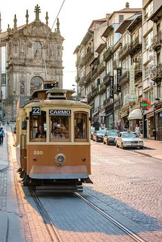 an orange trolley car traveling down a street next to tall buildings and people walking on the sidewalk