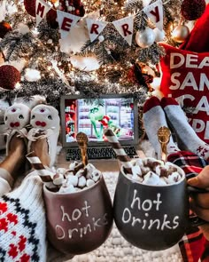 two people sitting in front of a christmas tree with hot drinks and marshmallows