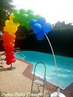 a rainbow colored balloon arch next to a swimming pool