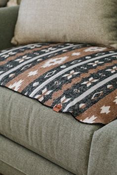 a brown and black patterned blanket sitting on top of a green couch next to pillows