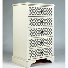 a white dresser with four drawers and an intricate design on the top drawer, in front of a gray background