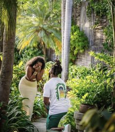 two women in white shirts and green pants are talking on their cell phones while walking through the jungle