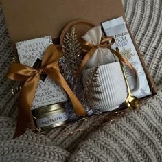 a gift box with candles, tea and cookies in it on a bed next to a knitted blanket