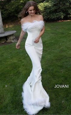 a woman in a white gown walking through the grass with her hand on her hip