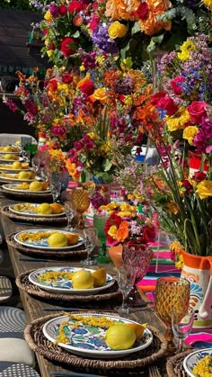 a long table with many plates and bowls on it that has flowers in the background